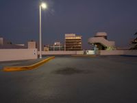 a empty parking lot near a building in the distance at night with street lights shining above the buildings