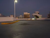 a empty parking lot near a building in the distance at night with street lights shining above the buildings