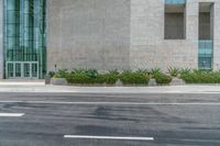 the curb in front of a grey wall with planters and grass growing on it