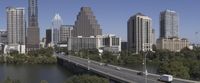 cars on a highway in front of skyscrapers over a river surrounded by trees and skyscrapers