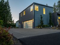 a gray and blue two story house in the evening light by some trees and plants