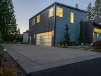 a gray and blue two story house in the evening light by some trees and plants