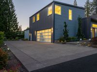 a gray and blue two story house in the evening light by some trees and plants