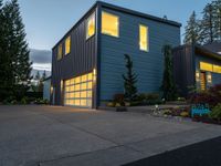 a gray and blue two story house in the evening light by some trees and plants