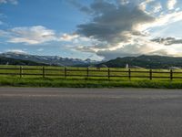 the road is empty during the day and has mountains in the distance as well as a fence