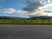 the road is empty during the day and has mountains in the distance as well as a fence