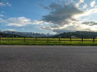 the road is empty during the day and has mountains in the distance as well as a fence