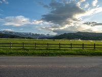 the road is empty during the day and has mountains in the distance as well as a fence