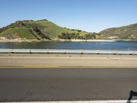 a road and a body of water near a bridge in the background of mountains and water