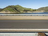 a road and a body of water near a bridge in the background of mountains and water