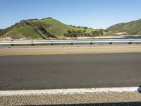 a road and a body of water near a bridge in the background of mountains and water