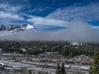 the view looking toward a mountain that is covered in snow and fog above it is some small village