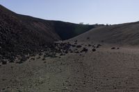 a herd of animals grazing on top of a hill of dirt with mountains in the background