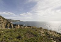 the person is on the edge of the cliff watching the water, rocks and grass