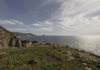 the person is on the edge of the cliff watching the water, rocks and grass