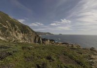 the person is on the edge of the cliff watching the water, rocks and grass