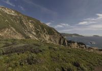 the person is on the edge of the cliff watching the water, rocks and grass