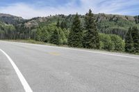 there is an empty highway on the mountain side with mountains in the background during daytime