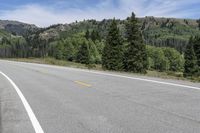 there is an empty highway on the mountain side with mountains in the background during daytime