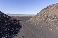 an empty dirt road running between a barren hill and a dirt patch on either side