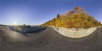 a fish eye view of a wide open road, with a wall surrounding it, and an autumn tree behind