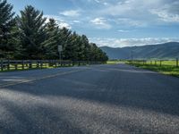 a empty road that goes through a grassy area with mountains in the background as well as trees