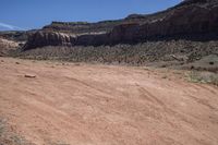 a dirt road through a desert plain with a mountain behind it and a clear blue sky in the background