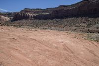 a dirt road through a desert plain with a mountain behind it and a clear blue sky in the background