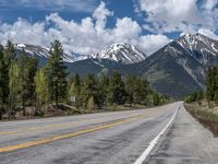 road in the mountains with pine trees and mountains in the background with blue sky with fluffy clouds