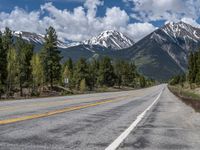 road in the mountains with pine trees and mountains in the background with blue sky with fluffy clouds