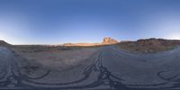 the panoramic image shows some sort of desert with rocks in the distance and on each end a long path is surrounded by grass