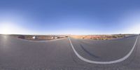 the panoramic image shows some sort of desert with rocks in the distance and on each end a long path is surrounded by grass