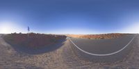 the panoramic image shows some sort of desert with rocks in the distance and on each end a long path is surrounded by grass