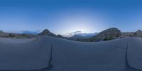 the panoramic image shows some sort of desert with rocks in the distance and on each end a long path is surrounded by grass