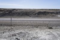 a dirt road is surrounded by some hills and desert like terrain as the vehicle sits on it