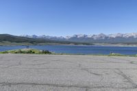 a man on a street riding a bike on a road that has lake behind him