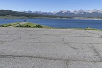 a man on a street riding a bike on a road that has lake behind him