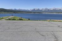 a man on a street riding a bike on a road that has lake behind him