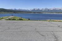 a man on a street riding a bike on a road that has lake behind him