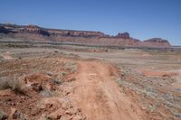 a dirt road through a desert plain with a mountain behind it and a clear blue sky in the background