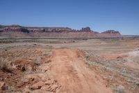 a dirt road through a desert plain with a mountain behind it and a clear blue sky in the background