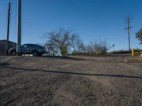 a car sitting next to some telephone poles in a dirt road by a pole that is over looking the other way