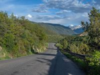 the road winds up on the mountainside on a sunny day with beautiful clouds and trees