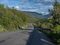 the road winds up on the mountainside on a sunny day with beautiful clouds and trees