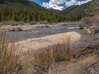 an image of a field that has snow on the mountain top in the background and a stream running through the forest