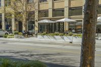 people sit outside an outdoor restaurant with umbrellas in the sunshine over the tables and chairs