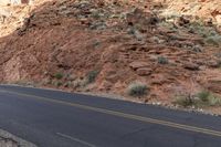 two people on their motorbikes are going down the road on the street in front of rocks and shrubs