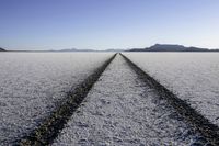 an empty dirt road is shown with snow on it and mountains in the background along one side of the dirt field