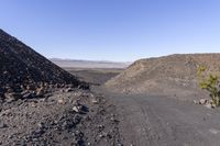 dirt road in desert landscape next to sparse plant on left side and mountain at right