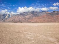 an image of a barren desert field with mountains in the background and blue sky above